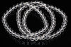 A clear quartz bracelet with round beads arranged in a loop on a dark reflective surface.