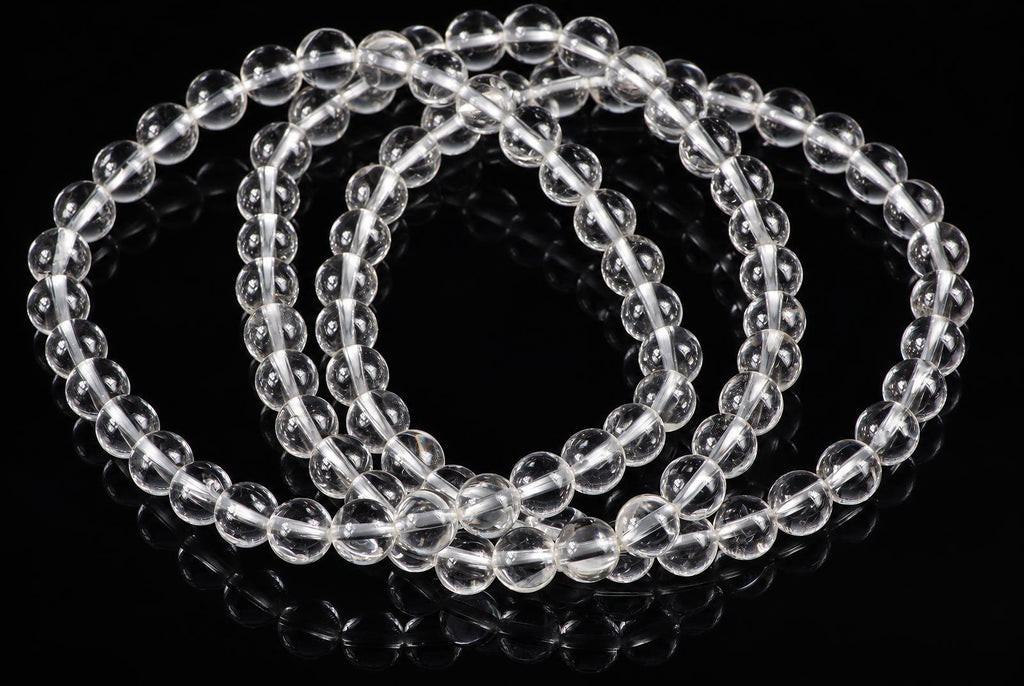 A clear quartz bracelet with round beads arranged in a loop on a dark reflective surface.