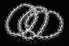 Three clear quartz bead bracelets arranged in loops on a dark reflective surface.