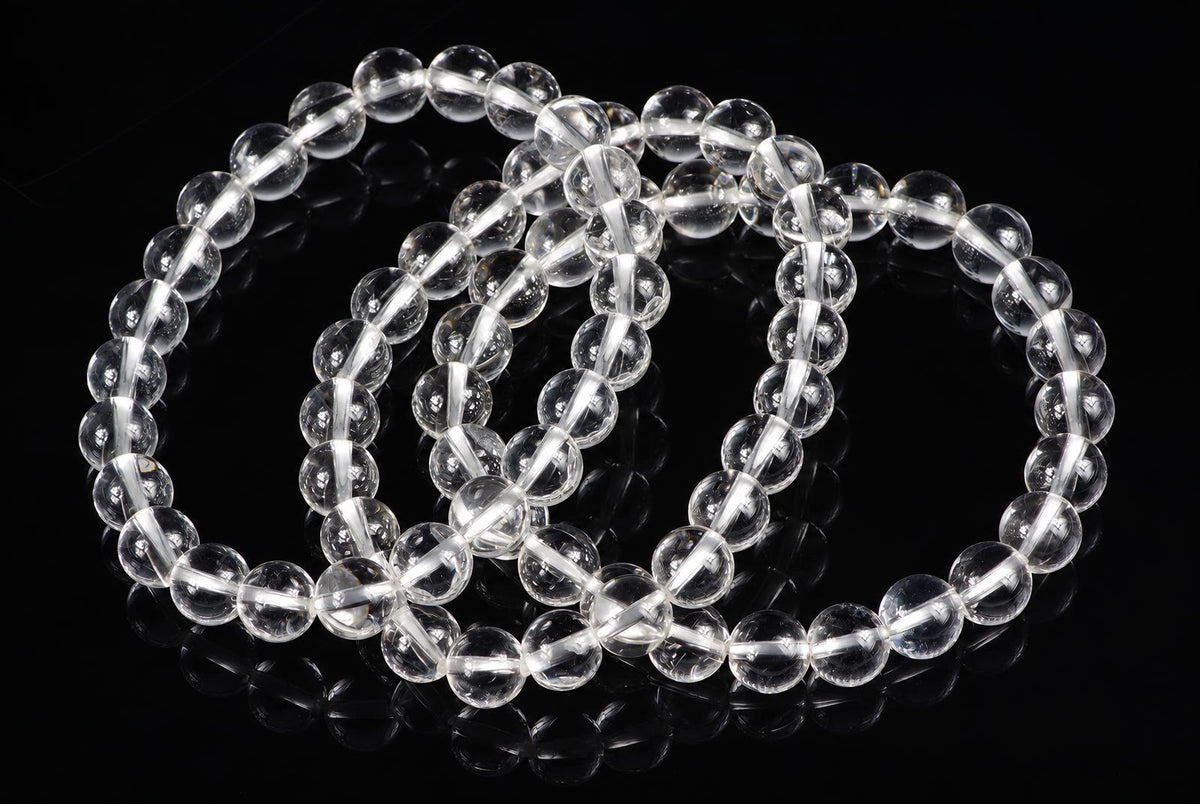 Three clear quartz bead bracelets arranged in loops on a dark reflective surface.