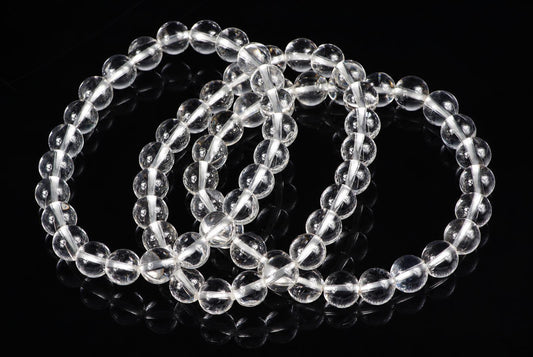 Three clear quartz bead bracelets arranged in loops on a dark reflective surface.
