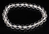 A bracelet of clear, round quartz beads on a dark surface.