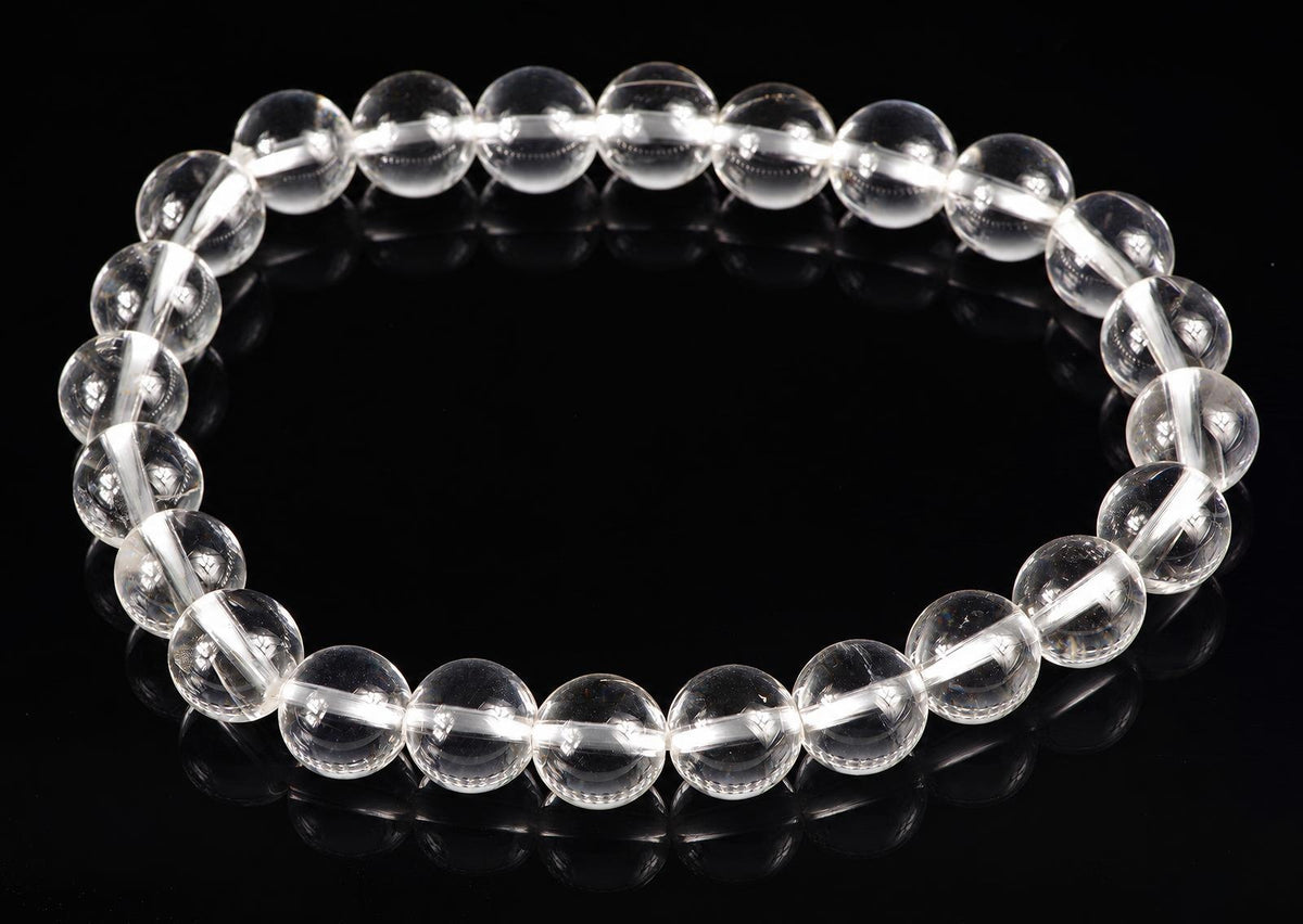 A bracelet of clear, round quartz beads on a dark surface.
