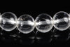 Four clear quartz beads with engraved floral patterns, arranged in a row on a dark reflective surface.