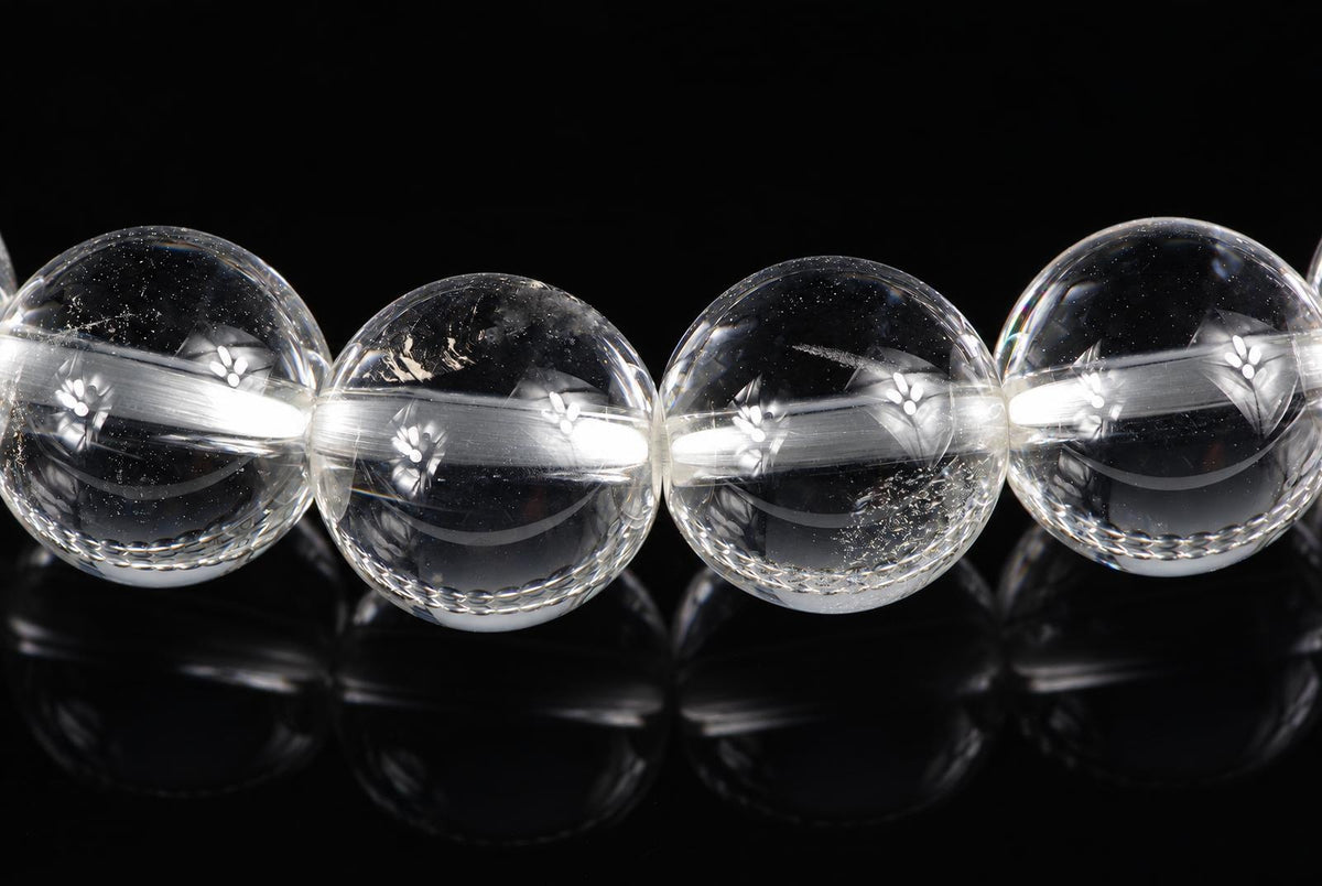 Four clear quartz beads with engraved floral patterns, arranged in a row on a dark reflective surface.