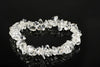 A bracelet made of clear, irregular quartz chips arranged in a circle on a dark reflective surface.