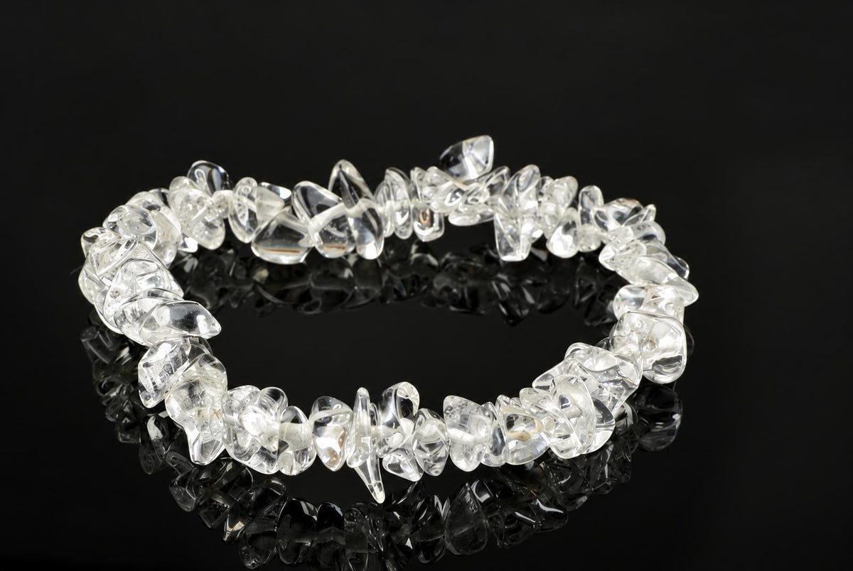 A bracelet made of clear, irregular quartz chips arranged in a circle on a dark reflective surface.