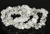 A bracelet made of clear, irregular quartz chips arranged in a loop on a dark reflective surface.