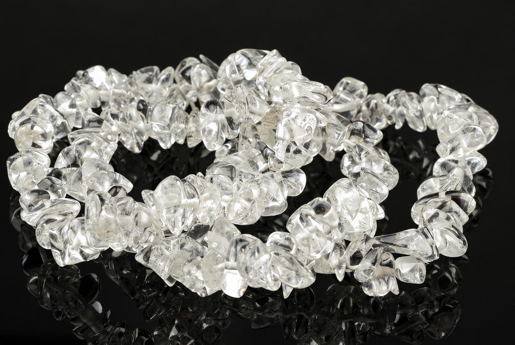 A bracelet made of clear, irregular quartz chips arranged in a loop on a dark reflective surface.