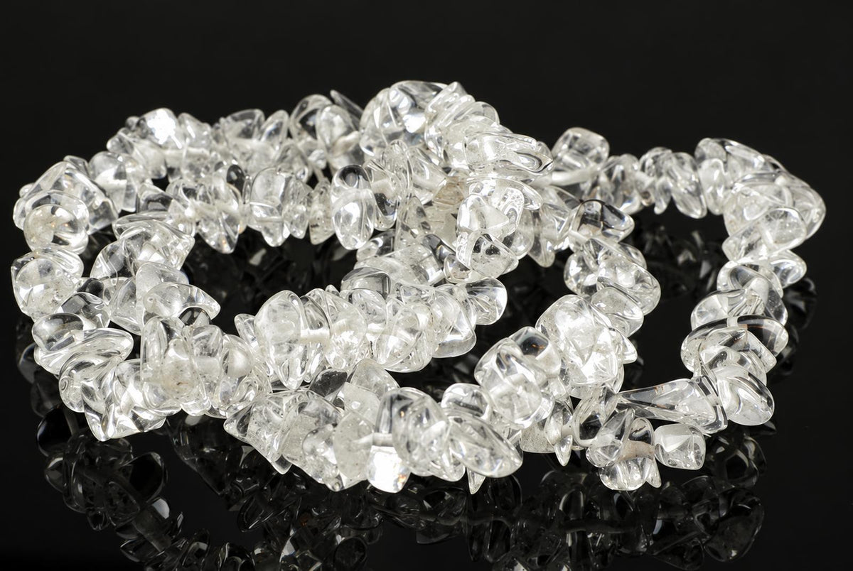 A bracelet made of clear, irregular quartz chips arranged in a loop on a dark reflective surface.