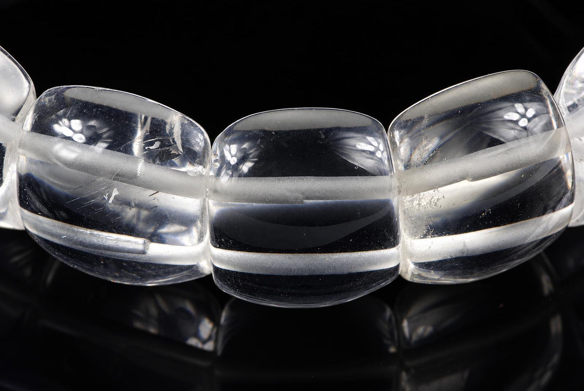 A close-up of a bracelet with large, clear quartz beads featuring frosted horizontal bands, set against a dark surface.