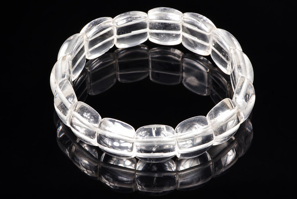 A clear quartz bracelet with smooth, rounded beads arranged in a circle on a dark reflective surface.