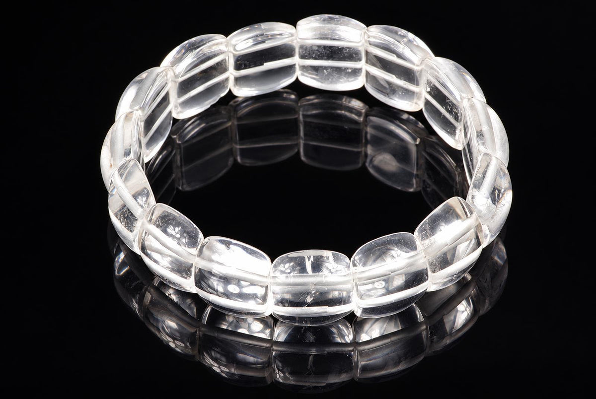 A clear quartz bracelet with smooth, rounded beads arranged in a circle on a dark reflective surface.