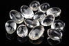 Twelve clear quartz stones with smooth, oval shapes arranged on a dark reflective surface.