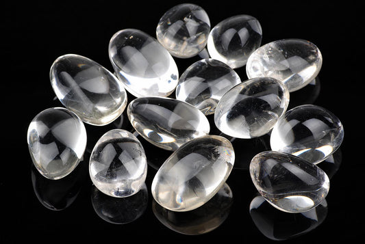 Twelve clear quartz stones with smooth, oval shapes arranged on a dark reflective surface.