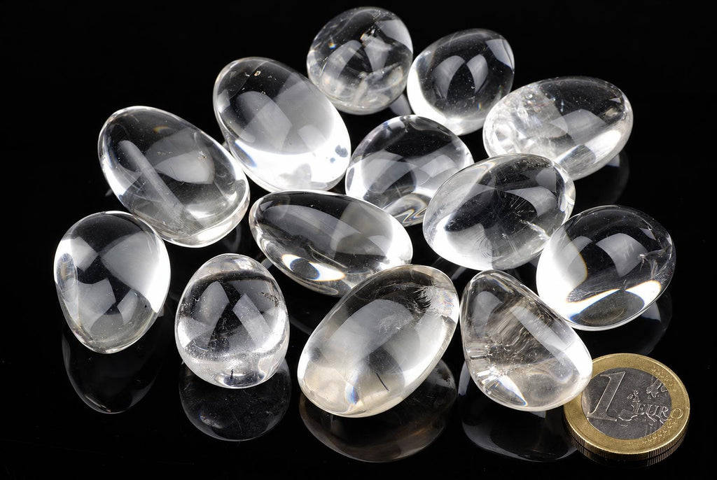Twelve clear quartz stones on a dark surface with a one euro coin for scale.