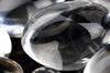 A close-up of a clear, smooth quartz crystal resting on a dark surface with other crystals nearby.