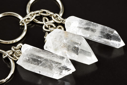 Three clear quartz crystal keyrings with silver-toned metal rings and chains on a dark surface.