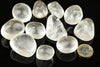 A group of smooth, clear quartz stones on a dark surface with a one-euro coin for scale.