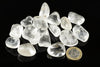 A pile of clear, translucent quartz stones on a dark surface with a one euro coin for scale.