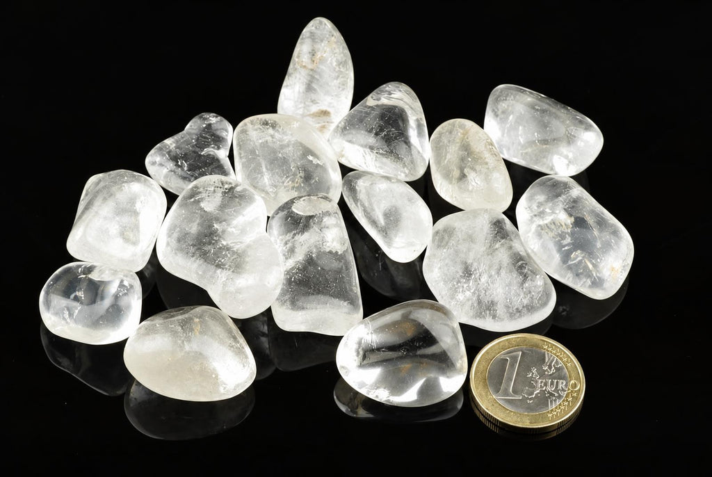 A pile of clear, translucent quartz stones on a dark surface with a one euro coin for scale.