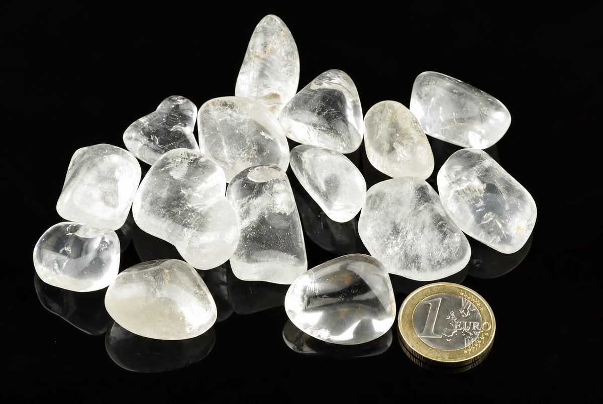 A pile of clear, translucent quartz stones on a dark surface with a one euro coin for scale.