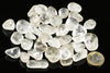 A pile of smooth, clear quartz stones on a dark surface with a one euro coin for scale.