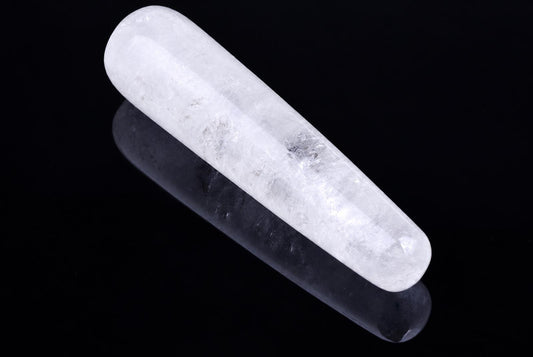 A polished, translucent white quartz massage stick with rounded ends rests on a dark reflective surface.