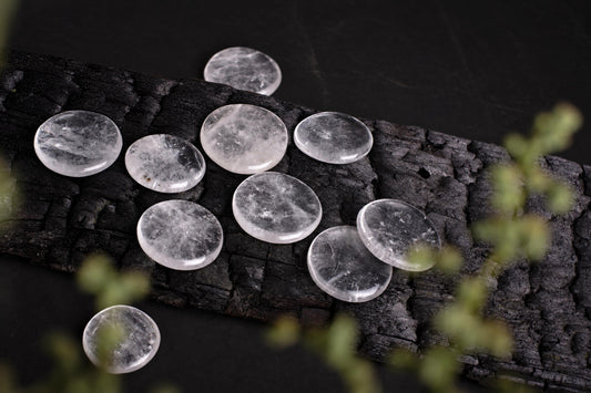 Several round, clear quartz palmstones with internal white inclusions rest on a dark, textured wooden surface.
