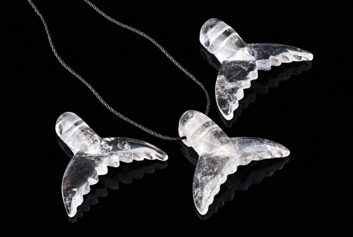 Three clear quartz dolphin-tail pendants on a dark cord, arranged diagonally on a black reflective surface.