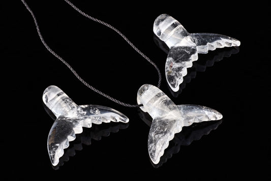 Three clear quartz dolphin-tail pendants on a dark cord, arranged diagonally on a black reflective surface.
