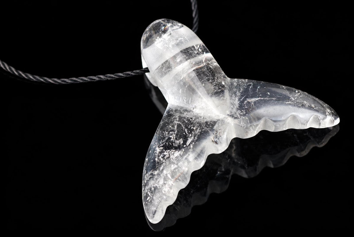 A clear quartz pendant shaped like a dolphin tail hangs from a dark cord against a black background.