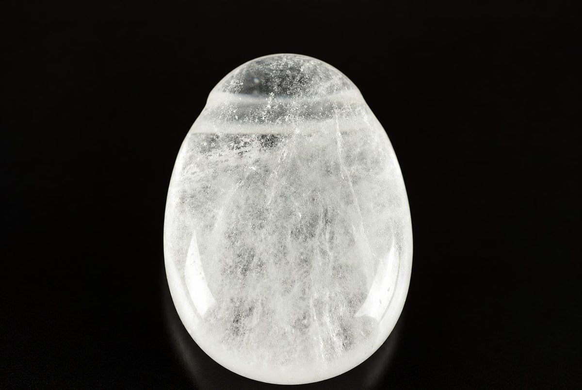 A polished, translucent white quartz pendant with internal inclusions, set against a dark surface.