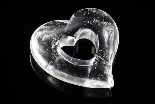 A clear, heart-shaped quartz pendant with a hollow center rests on a dark surface.