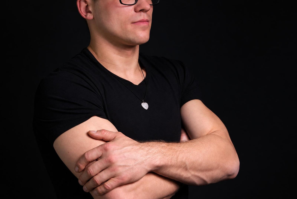 A man in a black t-shirt wears a white heart-shaped quartz pendant on a dark surface.