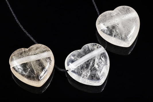Three heart-shaped quartz pendants with visible internal inclusions hang on dark cords against a black reflective surface.