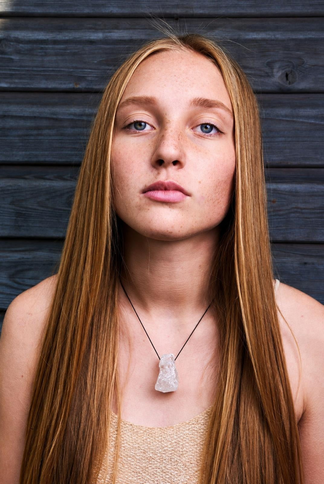 A woman wears a necklace with an irregular, translucent white quartz pendant on a black cord against a dark wooden background.