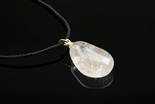 A translucent quartz pebble pendant with pale cloudy markings hangs from a black cord above a reflective dark surface.