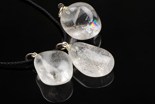 Three clear quartz pebble pendants with gold-toned fittings on black cords, resting on a dark reflective surface.