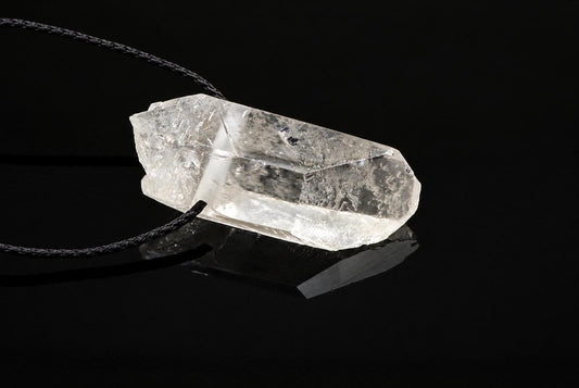A clear quartz crystal pendant with a dark cord rests on a dark surface.