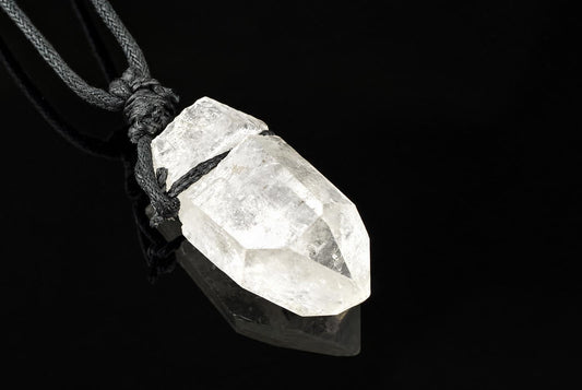 A clear quartz crystal pendant with a pointed tip, tied to a dark cord against a black background.