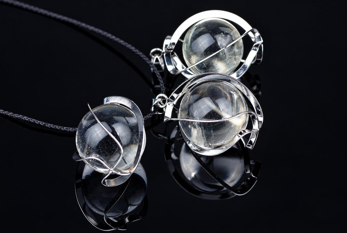 Three silver-toned wire pendants with clear quartz spheres on black cords, arranged on a dark reflective surface.