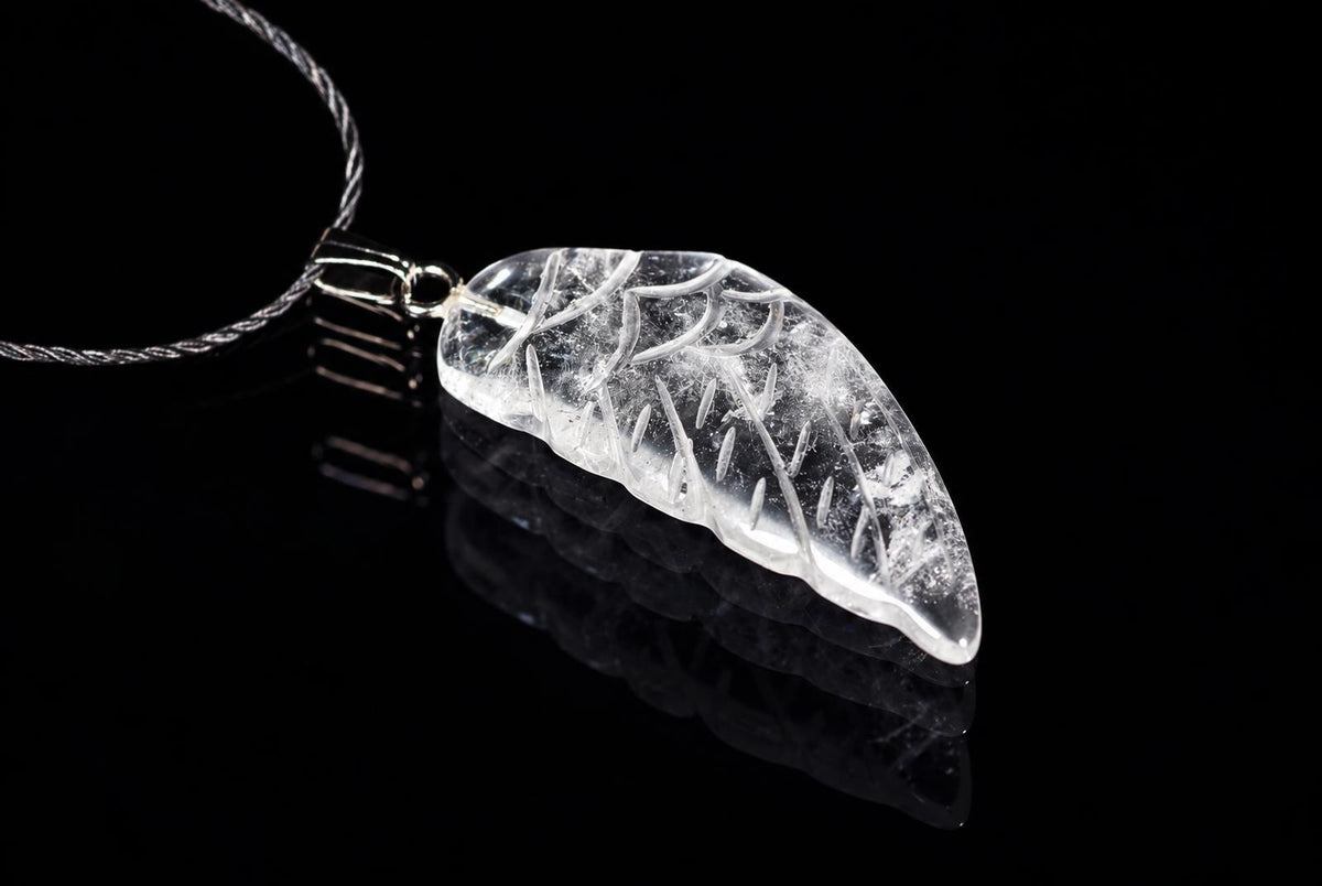 A clear quartz pendant shaped like a wing with white inclusions, attached to a silver-toned cord on a dark reflective surface.