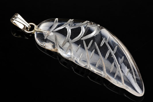 A silver-toned pendant with a clear, leaf-shaped quartz body featuring engraved vein-like lines, set against a dark reflective surface.