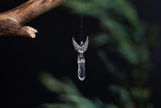 A silver-toned wing pendant with a clear quartz crystal hangs from a black cord against a dark background.