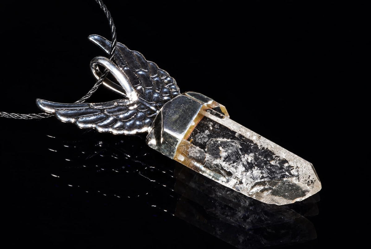 A silver-toned pendant with wing details holds a clear quartz crystal on a dark reflective surface.