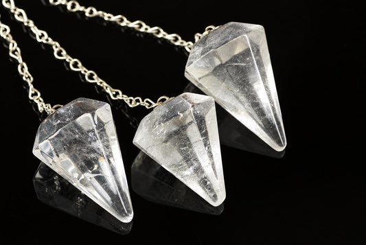 Three clear quartz point pendants on silver-toned chains rest on a dark, reflective surface.