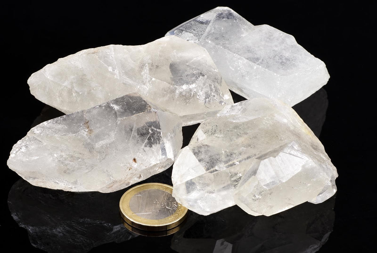 Four clear quartz crystals on a dark surface with a one euro coin for scale.