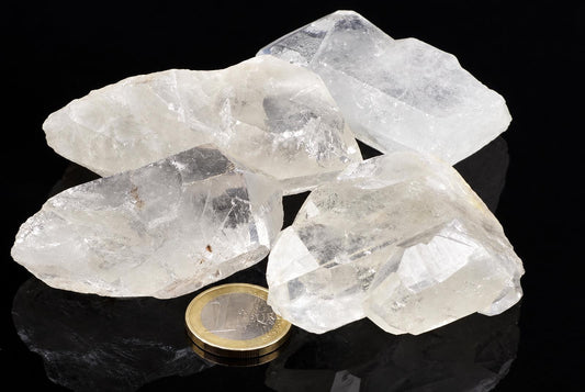 Four clear quartz crystals on a dark surface with a one euro coin for scale.