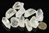 A group of clear, translucent quartz crystals with pointed tips arranged on a dark surface next to a one-euro coin.